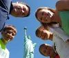 A family of five is smiling at the camera with the Statue of Liberty in the background captured from a low angle