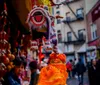 A colorful Chinese lion dance costume is hanging among other festive decorations in a bustling street market scene with a blurred view of onlookers in the background