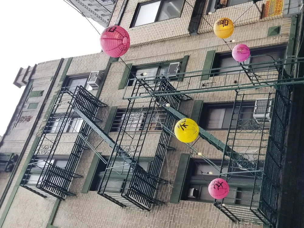 Colorful lanterns are strung across the facade of a building with a fire escape highlighting a festive or cultural decoration scheme