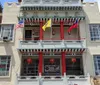 A colorful Chinese lion dance costume is hanging among other festive decorations in a bustling street market scene with a blurred view of onlookers in the background