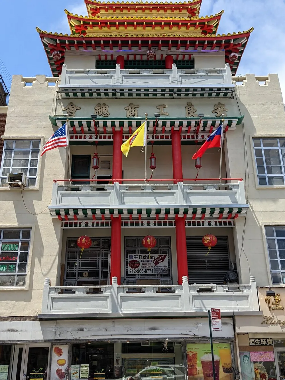 The image shows a multi-tiered building with an East Asian architectural style featuring American and Taiwanese flags hanging from the balcony against a clear sky