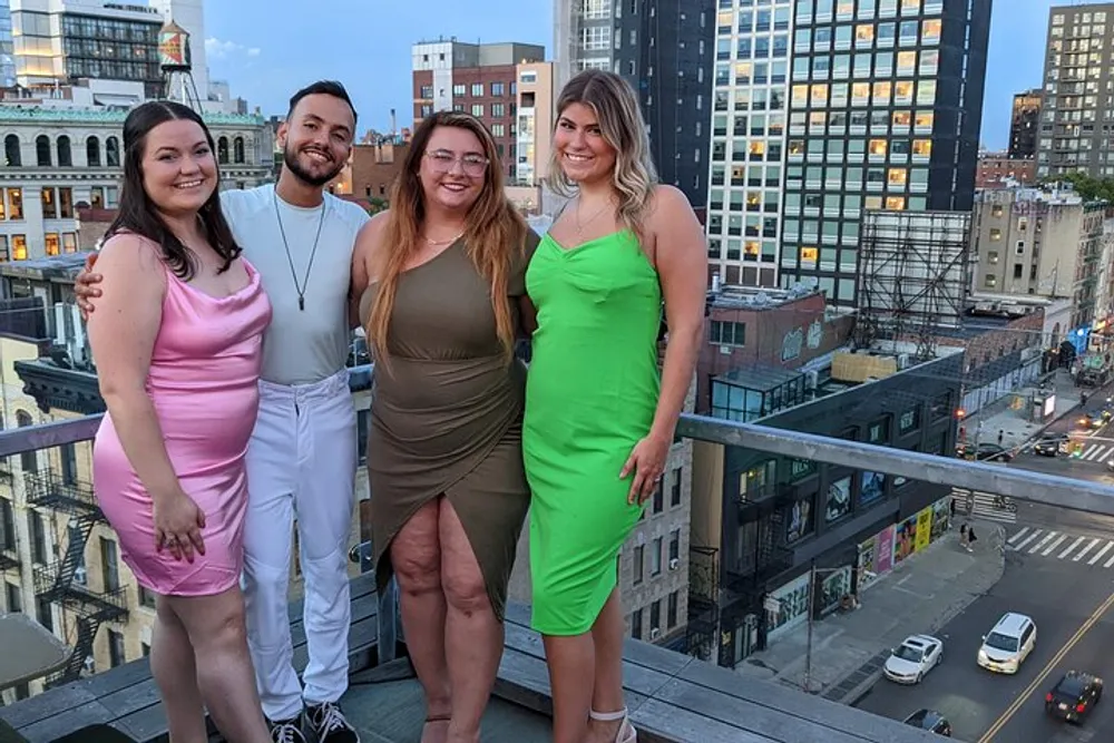 Four friends are smiling for a photo on a rooftop with a view of city buildings in the background