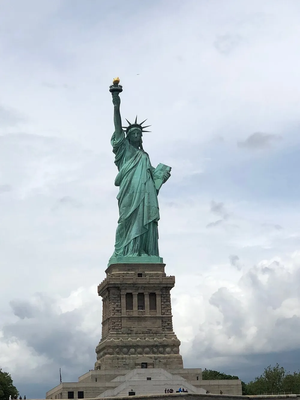 The image shows a close-up view of the Statue of Liberty against a cloudy sky background