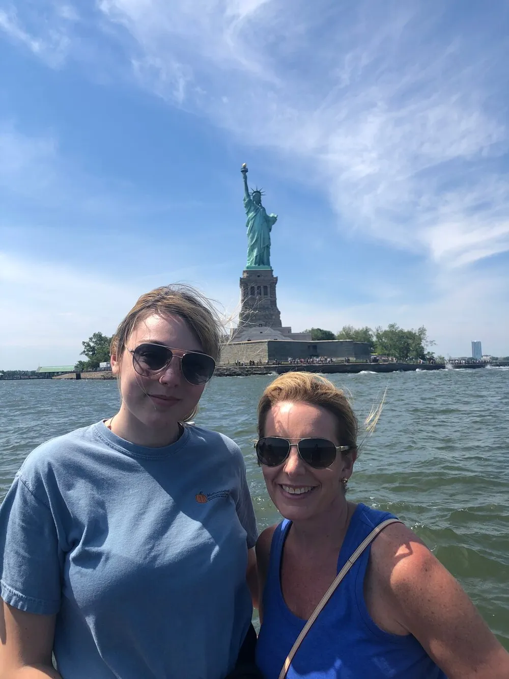 Two people are posing for a photo with the Statue of Liberty in the background